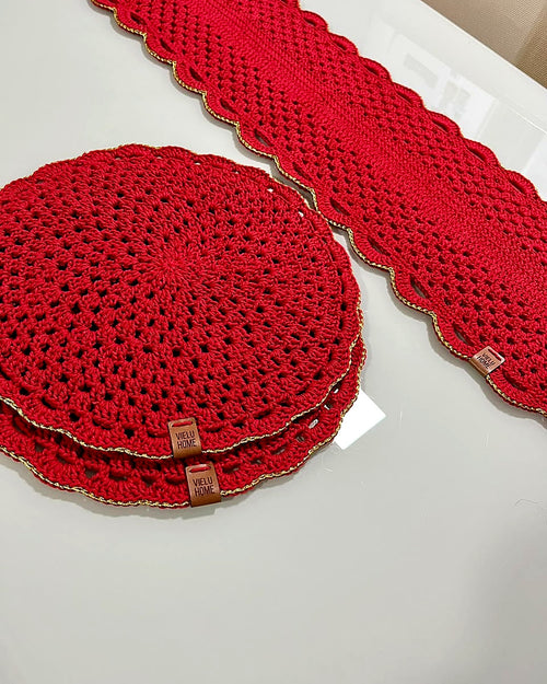 Sousplats de crochê vermelho empilhados ao lado do caminho de mesa